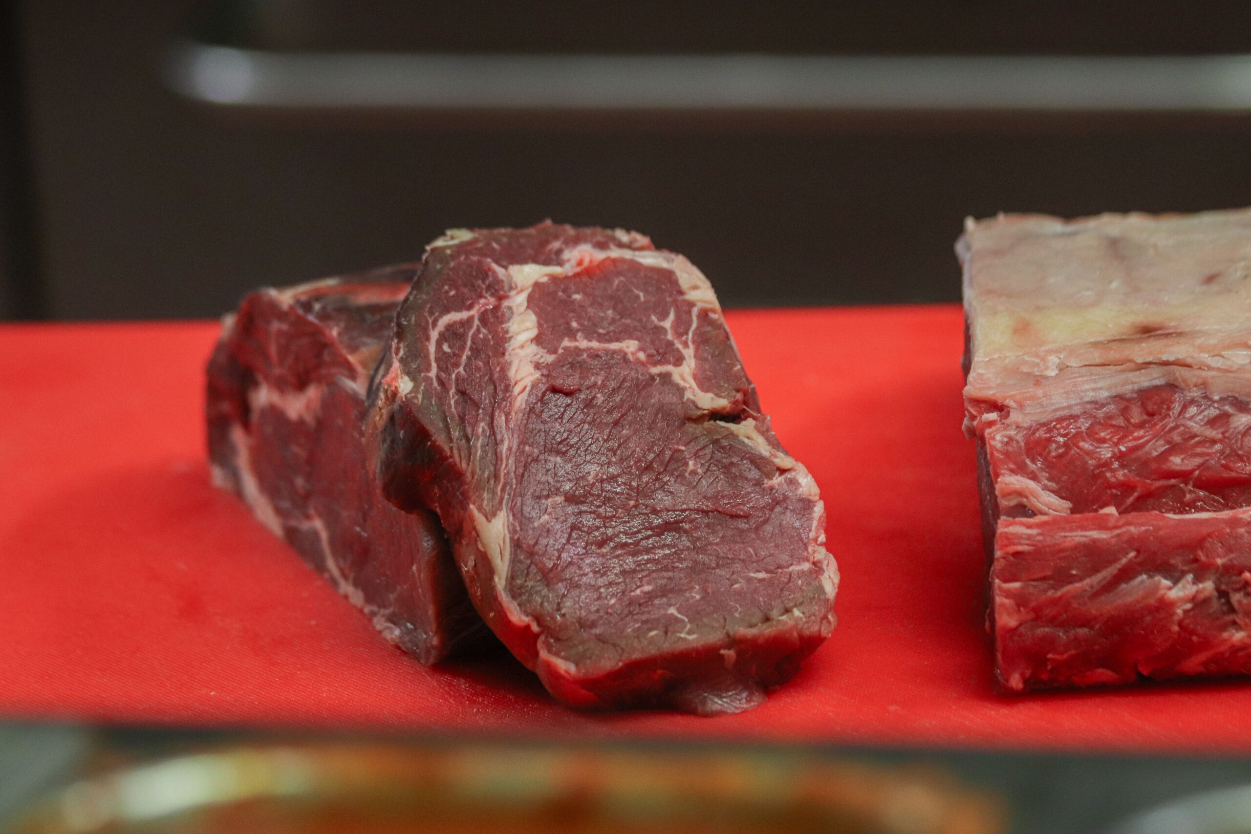 Close-up of raw beef pieces on a red cutting board, showcasing marbling and texture.